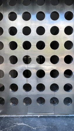 Close-up view of a metal surface with a regular pattern of circular perforations, creating a modern,...
