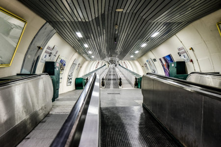 A wide, empty escalator tunnel in a modern underground metro station, with a long perspective creating a sense of depth and urban travel. High quality photoの写真素材