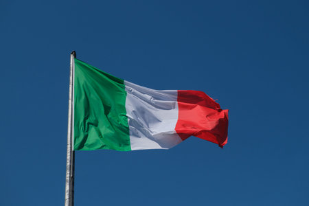 The Italian tricolor flag, with its green, white, and red stripes, waves gracefully in the wind...