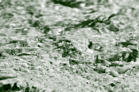 High-contrast, desaturated close-up of a rough submerged surface seen through rippling water, creating an abstract and mesmerizing optical effect. High quality photoの写真素材