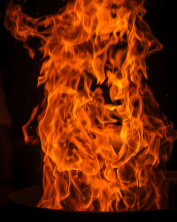A dramatic, close-up shot of a towering, intense column of fire, with vivid orange and yellow flames...
