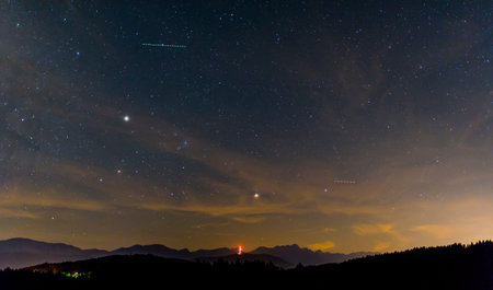 A long-exposure photograph of a vast, star-filled night sky with visible star trails and planets,...