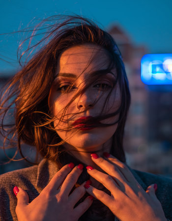 A moody, cinematic close-up of a woman's face. Her windblown hair covers her eyes, and she is lit by artistic blue and orange lights against a bokeh background. High quality photoの素材