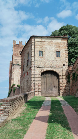 A steep red-brick path leads to a stone building with an arched entrance, flanked by medieval walls and a bell tower, evoking timeless European architecture. High quality photoの写真素材