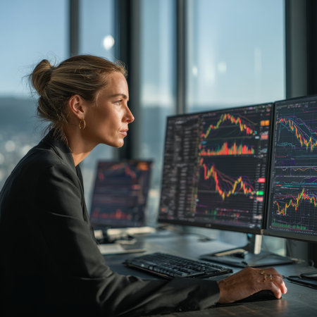 Individual seated at a modern desk analyzing multiple screens displaying stock market charts and financial data in a bright office setting. High quality photoの素材