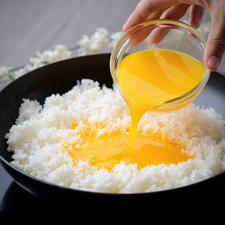 Detailed food shot showing fresh egg yolk being poured onto a bowl of steamed white rice, creating a rich and appetizing culinary composition. High quality photoの素材