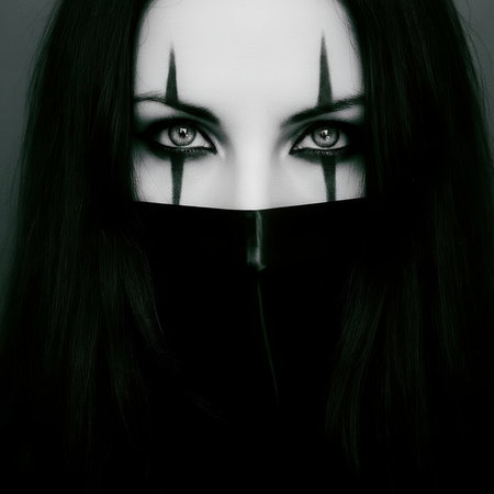 Close-up of a mysterious artistic portrait featuring intense black eye makeup and a dark hooded garment against a moody background. High quality photoの素材
