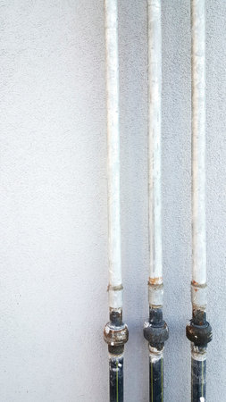 Three Vertical Metal Pipes Against Wall, Aged Galvanized Joints And Rusted Fittings Forming Textured