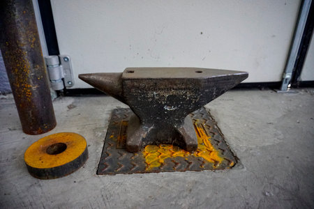 Rusty Anvil On Concrete Floor With Yellow Painted Weight And Rusted Pipe Nearby, Diamond Plate Base...