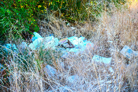 Piled Plastic Waste Among Dry Grass, Scattered Single Use Bags And Bottles Along Overgrown Bushes,...