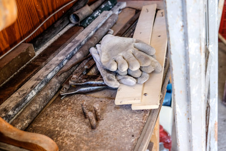 Worn work gloves resting on a dusty wooden workbench surrounded by hand tools and materials,...