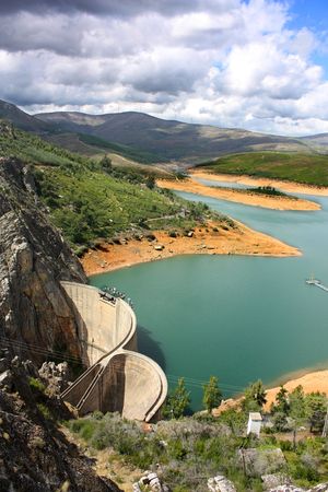 Aerial view of a water dam with a blue green lake and cloudy skyの写真素材