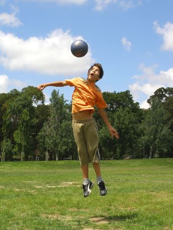 Boy playing soccer in a gree grass field with blue sky aboveの写真素材