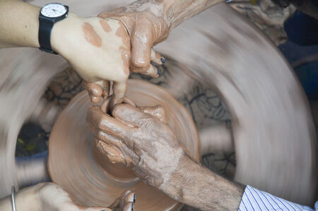 Making clay pot with hands shaping up the pot while the wheel is spinning の写真素材