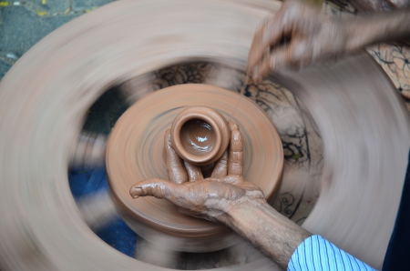 Making clay pot with hands shaping up the pot while the wheel is spinning の写真素材