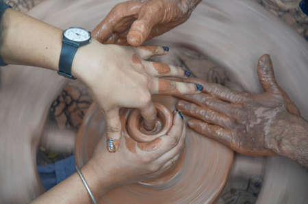 Making clay pot with hands shaping up the pot while the wheel is spinning の写真素材