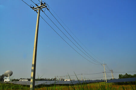 Electricity Pole standing tall in the green field against blue sky with solar panels and satellite at the backgroundの写真素材