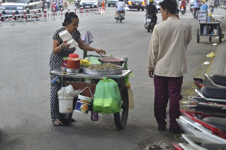 Ho Chi Minh City, Vietnam - October 2013 - Street vendor selling snack from her push cart on the busy streetのeditorial素材