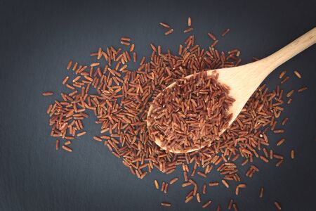 Raw Thai Jasmine Brown Rice in wood spoon on black slate plateの写真素材