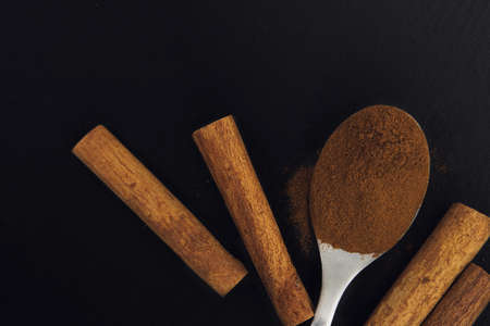 Cinnamon sticks and cinnamon powder in the tea spoon on black slate plateの写真素材