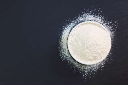 Wheat flour in white cup on black slate stone plate with copy space for preparing baking or pastaの写真素材