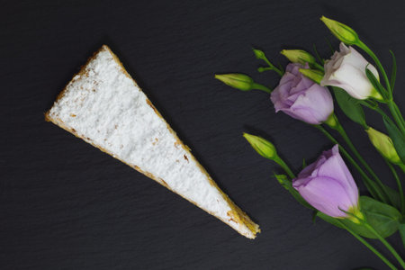 Classic French white praline layer cake decorate by violet flowers on black slate stone plate
