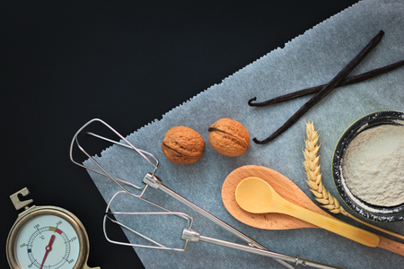 Bakery preparation tools wooden spoon, vanilla, thermometer, bake paper on black backgroundの写真素材