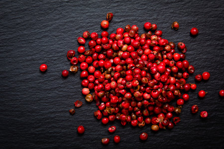 Organic peppercorn or pink pepper in iron scoop on black slate stone background