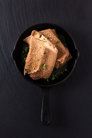Food concept homemade Ham and Cheese Crepe in iron skillet cast on black slate backgroundの写真素材