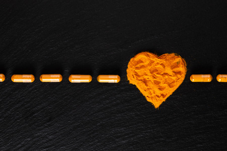 Health care concept Turmeric spices powder in heart shape and capsule in black backgroundの写真素材