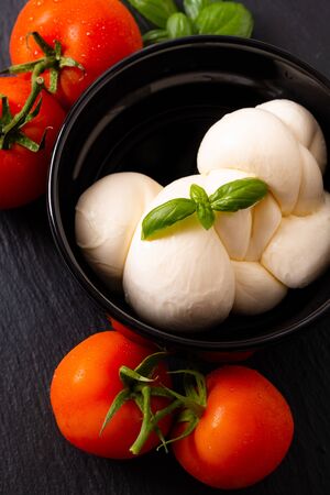 Food ingredient concept organic mozzarella cheese in black ceramic cup with  tomatoes and basil with copy spaceの写真素材