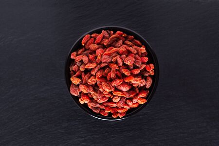Super brain food dry Goji berry in black ceramic cup on slate stone board with copy spaceの写真素材