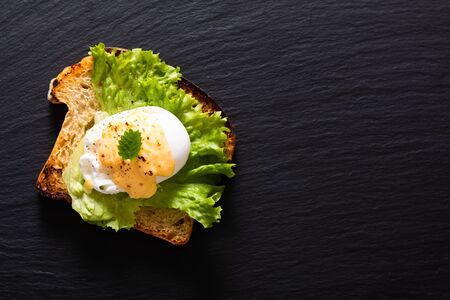 Organic Food breakfast concept homemade Poached egg or eggs benedict on sourdough bread toasted on black slate board の写真素材