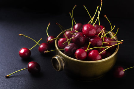 Summer food concept organic fresh cherry fruits in green cup on black slate board background with...