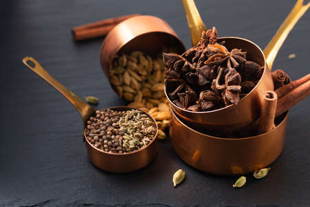 Food concept mix of masala spices, cinnamon, fennel, star anise, coriander seed and cinnamon pods in copper cup on black slate boardの写真素材