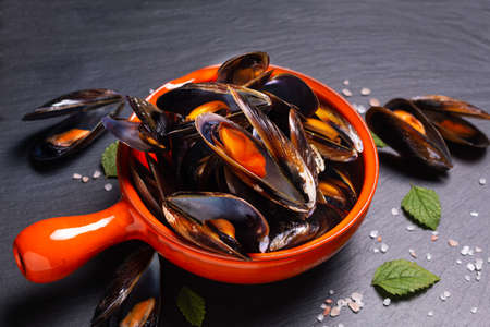 Seafood concept Mussels in orange handle bowl on black slate stone with copy spaceの写真素材