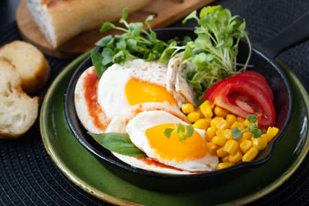 Fried eggs and micro-green salad with corn and tomato in Skillet iron panの写真素材