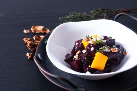 Food concept roasted Beetroot and butternut salad with goat cheese in white ceramic bowl on black...
