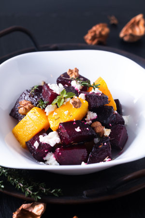 Food concept roasted Beetroot and butternut salad with goat cheese in white ceramic bowl on black...