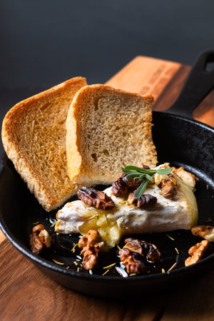 Food concept spot focus homemade Baked Brie cheese with honey and walnuts in skillet iron pan on wooden board with black slate stone copy spaceの写真素材