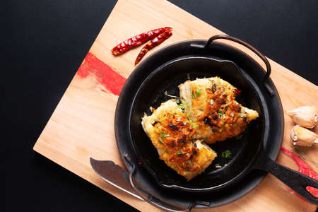 Food concept spot focus homemade butter, garlic, bread crumbs and cheese crunchy Baked cod fish in skillet iron cast pan on black background with copy spaceの写真素材