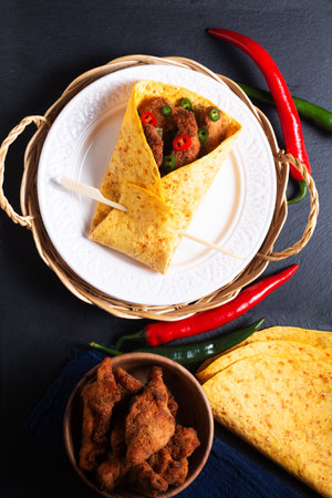 Food concept spicy Fried Chicken Tortilla Wrap with chopped chilies on black slate stone background...
