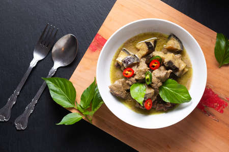 Thai Food concept homemade Thai Green curry in white ceramic bowl on wooden board and black slate stone background with copy spaceの写真素材