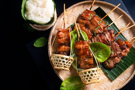 Thai street food concept Moo ping, Mu Ping, Thai-style grilled bbq pork skewers with rice stick on black background with copy spaceの写真素材