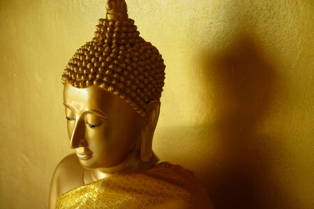A golden Buddha statue and his shadow on the golden wall の写真素材