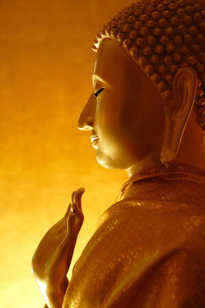 A golden Buddha in a teaching gesture on a golden background の写真素材