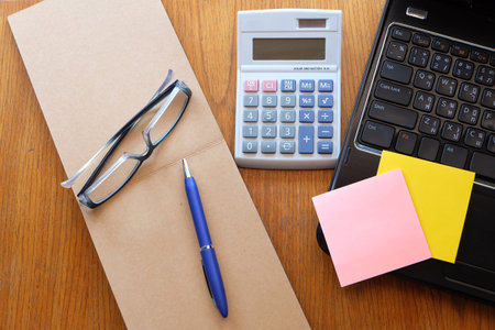 note book and laptop on wooden table with glasses and clock