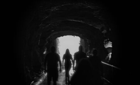 Silhouettes walking towards bright light as if passing over to the after life. Backlit black and white blurry image concept of death and moving on.の写真素材