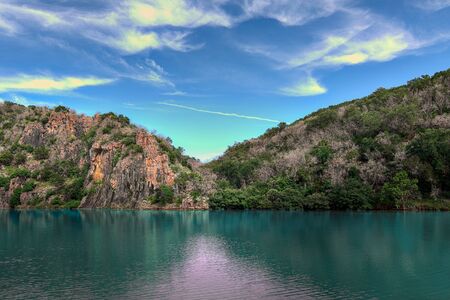 Iron stained cliffs behind Turquoise colored river in texas state park southwest america with whispy clouds in blue sky.の写真素材
