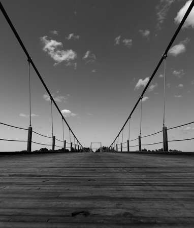 Low angle black white suspension bridge with clouds in sky wooden plank walkway traversing colorado river in Texas USA.の写真素材